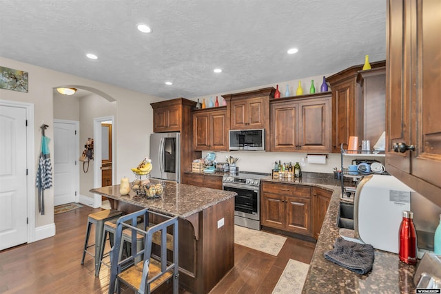 3308 Brickyard Ave, Rock Springs, WY 82901 - kitchen featuring appliances with stainless steel finishes, arched walkways, a kitchen breakfast bar, dark wood-style floors, and recessed lighting