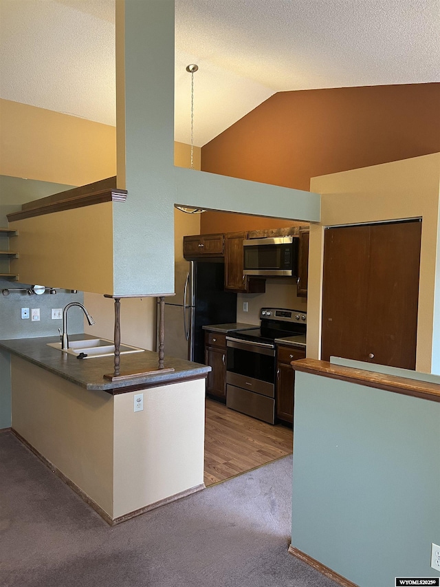 6358 Buckboard Rd, Casper, WY 82604 - kitchen featuring appliances with stainless steel finishes, dark countertops, a peninsula, carpet floors, and high vaulted ceiling