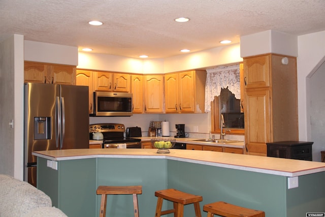 1540 Manor Dr, Casper, WY 82609 - kitchen with stainless steel appliances, light countertops, a textured ceiling, a breakfast bar area, and light brown cabinetry