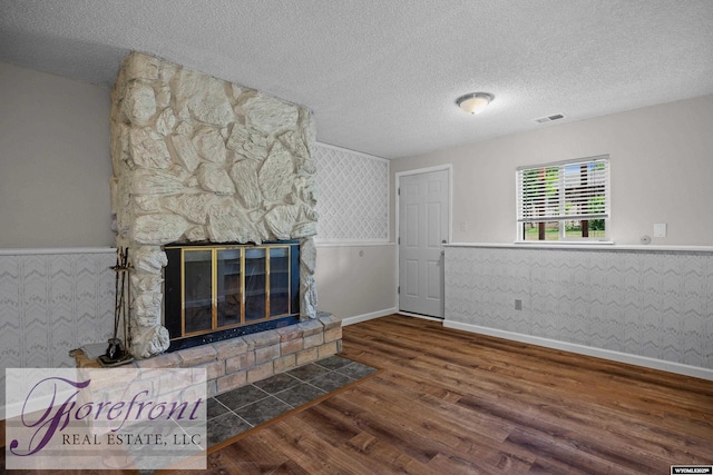 2240 E 17th St, Casper, WY 82609 - unfurnished living room with a wainscoted wall, wood finished floors, a textured ceiling, wallpapered walls, and a stone fireplace