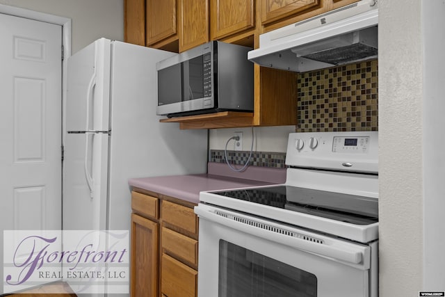 2240 E 17th St, Casper, WY 82609 - kitchen featuring white appliances, under cabinet range hood, tasteful backsplash, and brown cabinetry