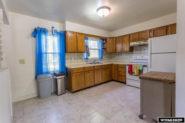 1220 Bon Ave, Casper, WY 82609 - kitchen featuring white appliances, under cabinet range hood, brown cabinetry, and light countertops