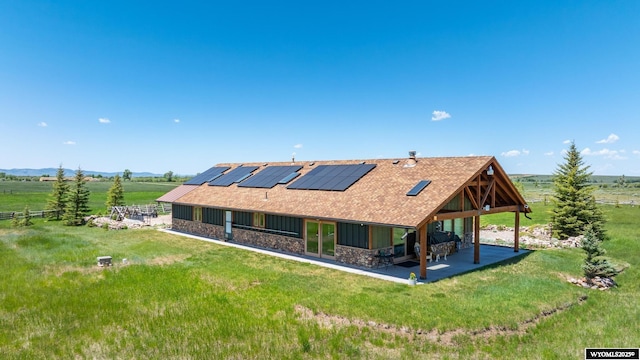 966 Mill Creek Rd, Evanston, WY 82930 - rear view of house featuring a patio area, stone siding, roof mounted solar panels, a yard, and a shingled roof