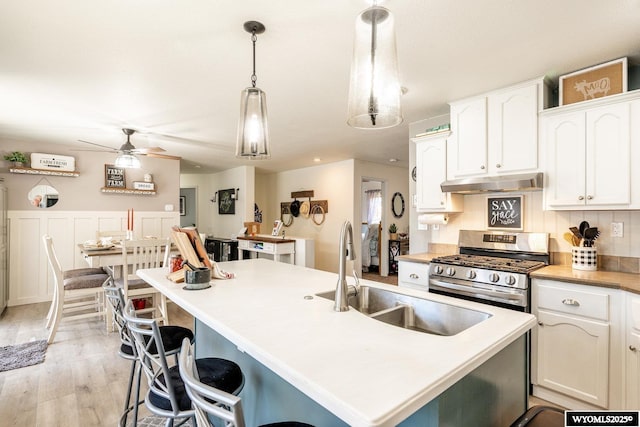 750 N Adams Ave, Buffalo, WY 82834 - kitchen featuring stainless steel gas range oven, under cabinet range hood, white cabinets, light wood-style floors, and a center island with sink
