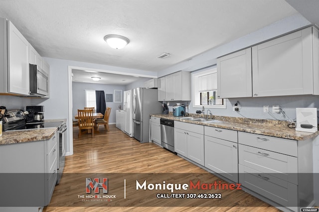 1043 Saint Mary St, Casper, WY 82601 - kitchen with appliances with stainless steel finishes, light wood finished floors, washer / clothes dryer, light stone countertops, and a textured ceiling