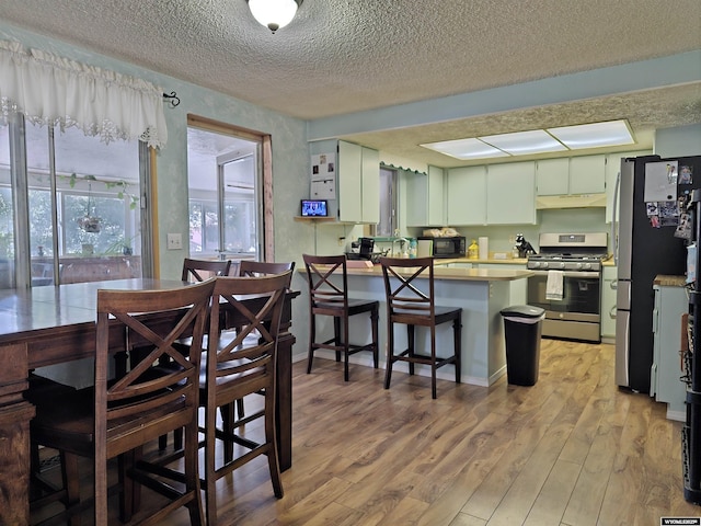 313 Cottonwood St, Evanston, WY 82930 - kitchen with stainless steel appliances, a textured ceiling, a peninsula, light wood-style floors, and under cabinet range hood
