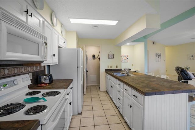 kitchen with tasteful backsplash, light tile patterned floors, a kitchen breakfast bar, white cabinets, and white appliances