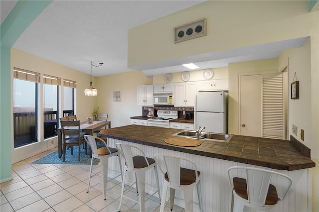 kitchen with white cabinetry, a breakfast bar, light tile patterned floors, hanging light fixtures, and white appliances