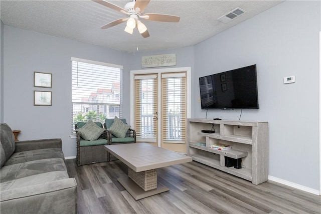 living area with baseboards, visible vents, a ceiling fan, wood finished floors, and a textured ceiling