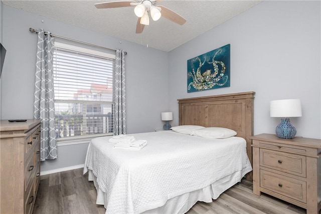 bedroom with a ceiling fan, a textured ceiling, baseboards, and wood finished floors