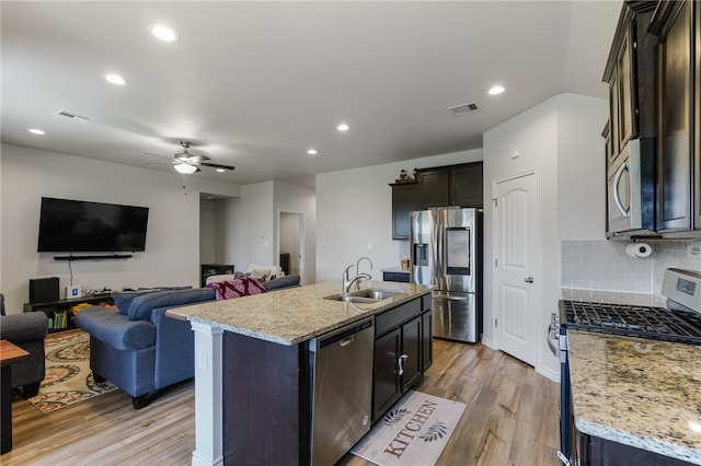 kitchen featuring stainless steel appliances, light stone counters, sink, an island with sink, and light hardwood / wood-style flooring