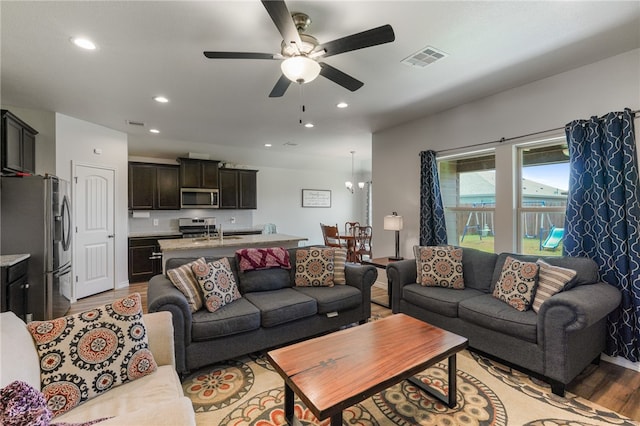 living room with ceiling fan with notable chandelier, light hardwood / wood-style floors, and sink