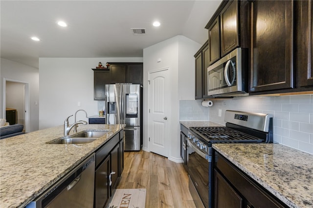 kitchen featuring stainless steel appliances, light stone counters, sink, tasteful backsplash, and light wood-type flooring