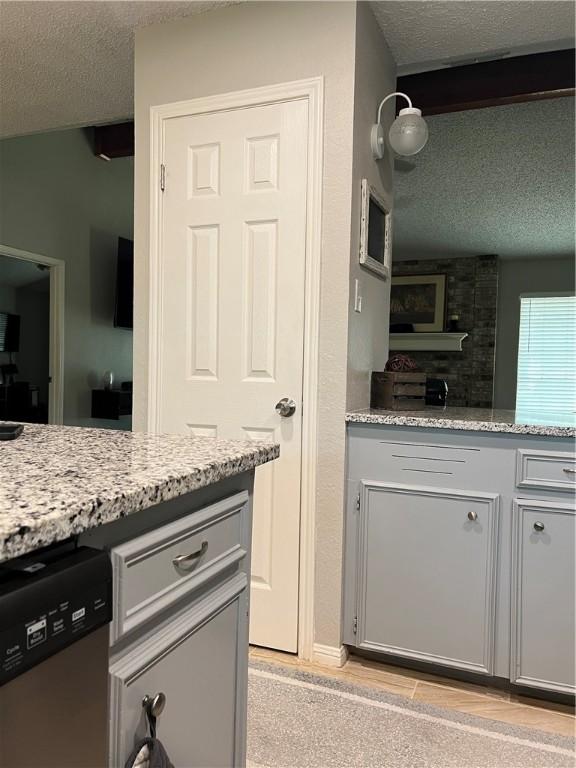 kitchen featuring light stone countertops, stainless steel dishwasher, and a textured ceiling