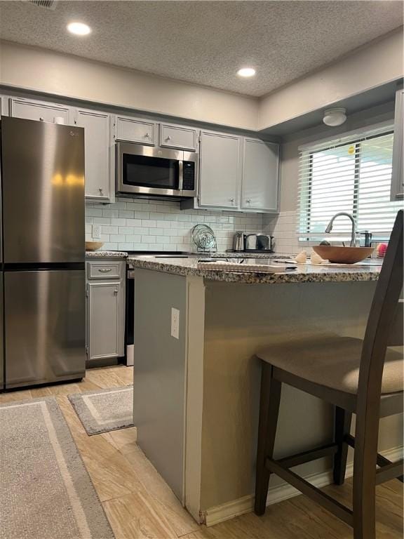 kitchen with a breakfast bar area, gray cabinetry, tasteful backsplash, dark stone counters, and stainless steel appliances