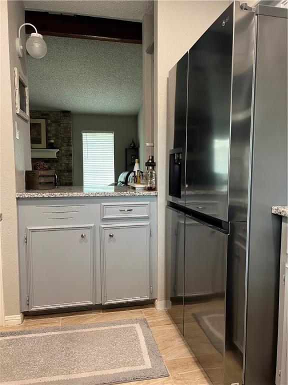 kitchen with light stone countertops, black refrigerator, gray cabinetry, and a textured ceiling