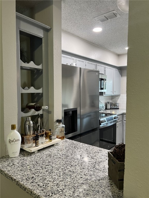 kitchen with a textured ceiling, appliances with stainless steel finishes, white cabinets, light stone countertops, and backsplash