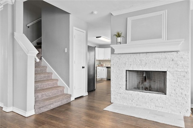 unfurnished living room with dark wood-type flooring, ornamental molding, and a stone fireplace