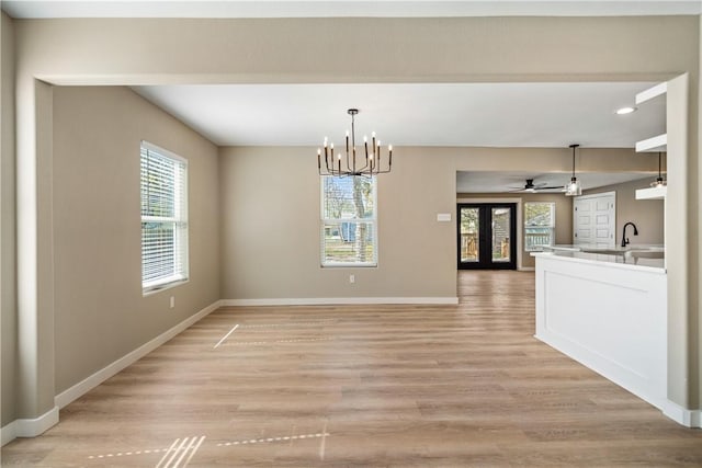 unfurnished dining area with light wood-type flooring, baseboards, and ceiling fan with notable chandelier