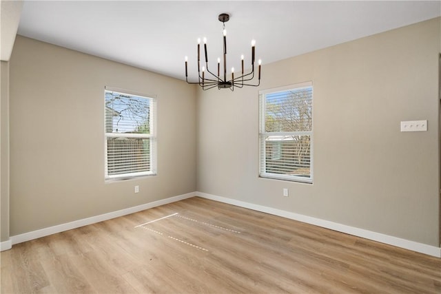 unfurnished room with a notable chandelier, a healthy amount of sunlight, baseboards, and light wood-type flooring