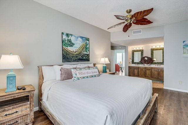 bedroom with a textured ceiling, dark hardwood / wood-style flooring, ceiling fan, and connected bathroom