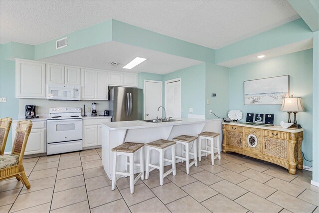 kitchen with white cabinetry, sink, a kitchen bar, a textured ceiling, and white appliances