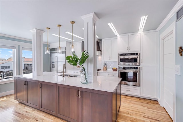 kitchen with pendant lighting, white cabinets, appliances with stainless steel finishes, light hardwood / wood-style floors, and decorative columns