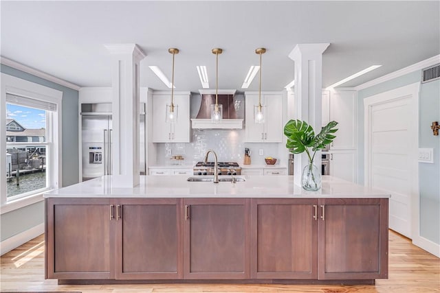 kitchen with a kitchen island with sink, light hardwood / wood-style flooring, white cabinets, and hanging light fixtures