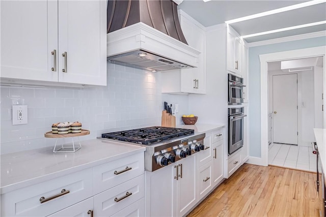 kitchen with white cabinetry, stainless steel appliances, light hardwood / wood-style flooring, premium range hood, and decorative backsplash