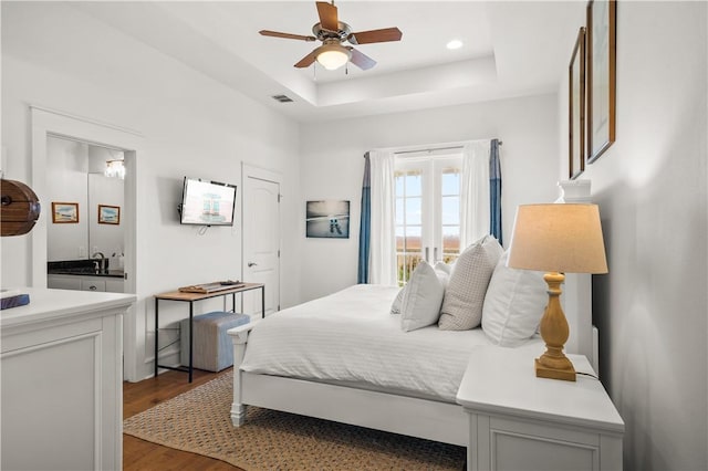 bedroom with visible vents, a tray ceiling, wood finished floors, recessed lighting, and french doors