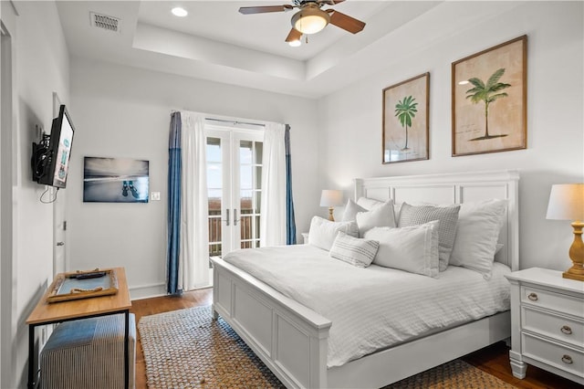 bedroom featuring visible vents, a tray ceiling, access to exterior, dark wood-type flooring, and french doors