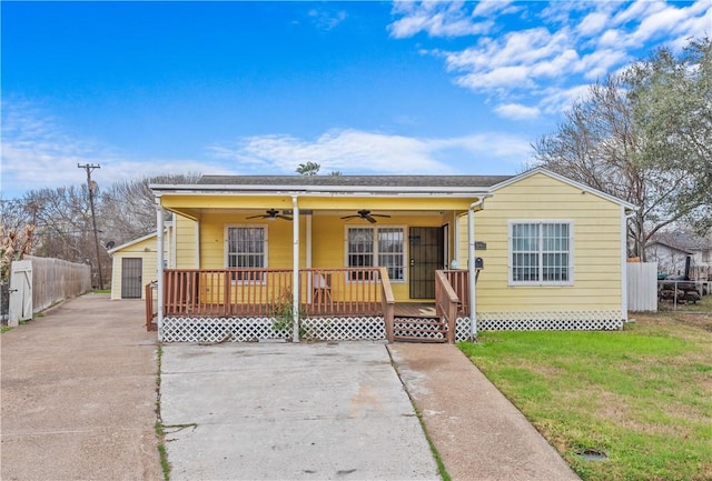 bungalow with a detached garage, covered porch, ceiling fan, fence, and a front lawn