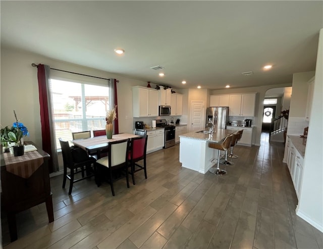 kitchen with appliances with stainless steel finishes, a kitchen breakfast bar, dark hardwood / wood-style floors, a kitchen island with sink, and white cabinets