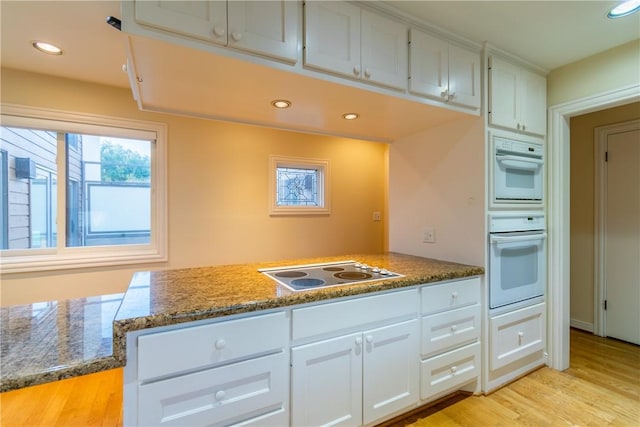 kitchen featuring electric stovetop, white cabinets, light hardwood / wood-style floors, and dark stone counters