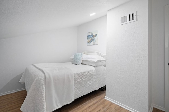 bedroom featuring baseboards, visible vents, wood finished floors, and a textured wall