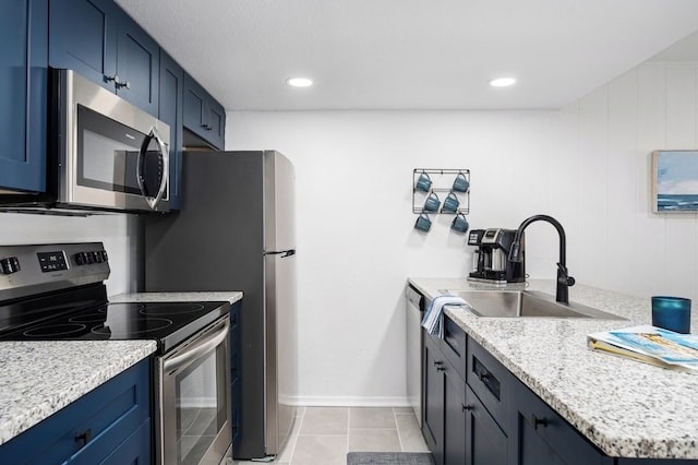 kitchen featuring light tile patterned floors, a sink, stainless steel appliances, blue cabinets, and baseboards