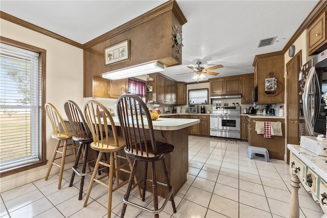 kitchen with ceiling fan, stainless steel range with electric stovetop, a breakfast bar area, light tile patterned floors, and ornamental molding