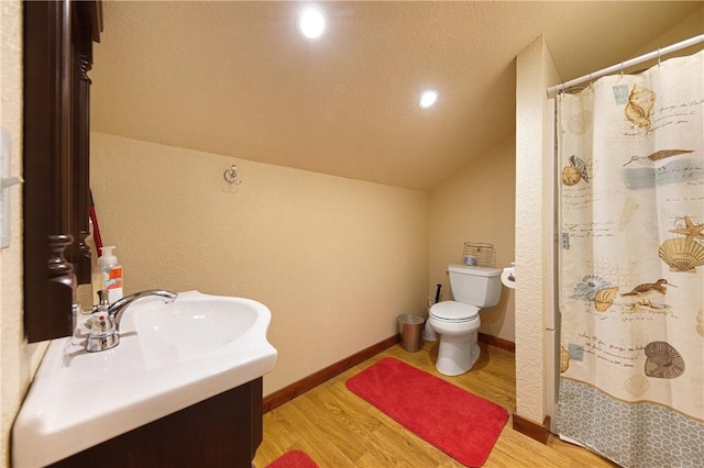 bathroom with vanity, toilet, wood-type flooring, and vaulted ceiling