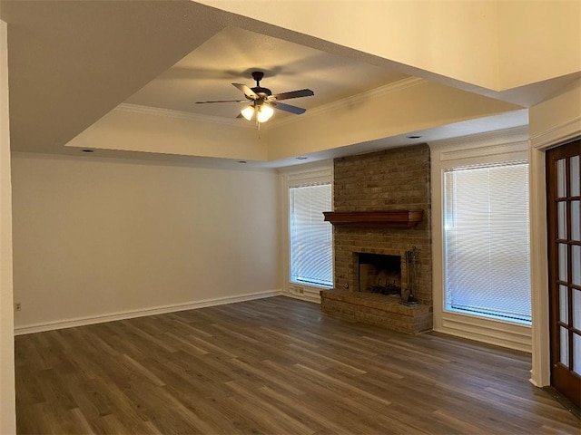 unfurnished living room featuring ornamental molding, a fireplace, a raised ceiling, dark wood-type flooring, and ceiling fan