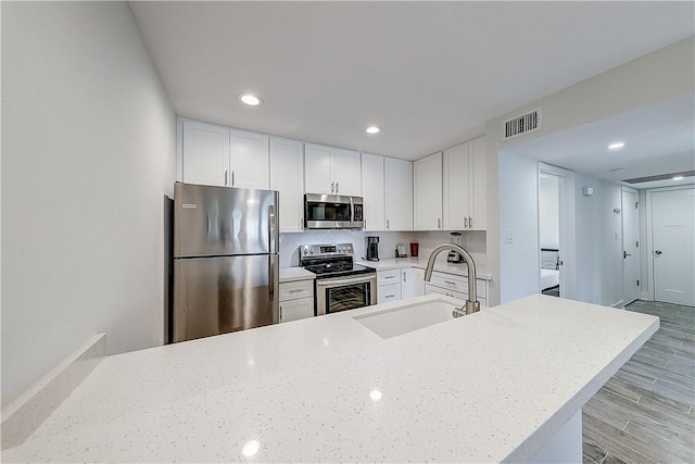 611 Lauderdale Dr, Rockport, TX 78382 - kitchen featuring stainless steel appliances, a sink, white cabinetry, light wood-style flooring, and light stone counters