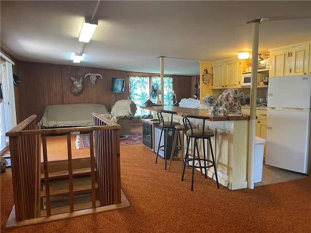 kitchen featuring a breakfast bar area, light carpet, decorative light fixtures, and white appliances