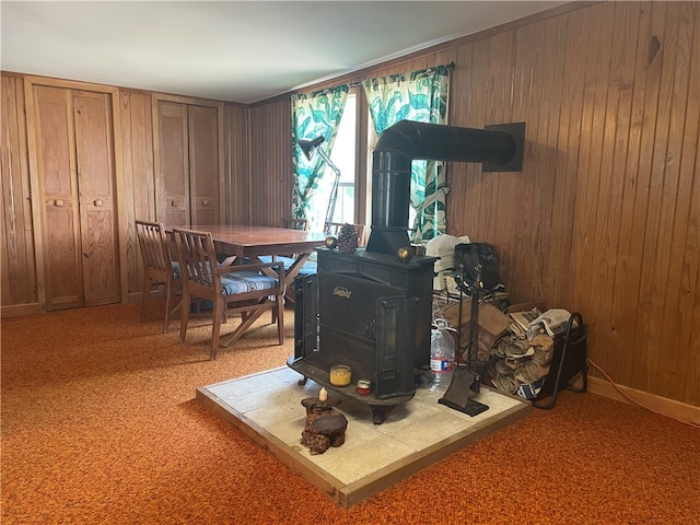 carpeted dining room with a wood stove and wood walls