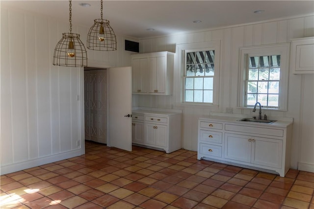 kitchen with a sink, white cabinetry, hanging light fixtures, and light countertops