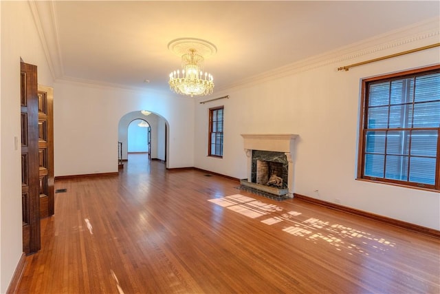 unfurnished living room featuring baseboards, a chandelier, a stone fireplace, wood finished floors, and arched walkways