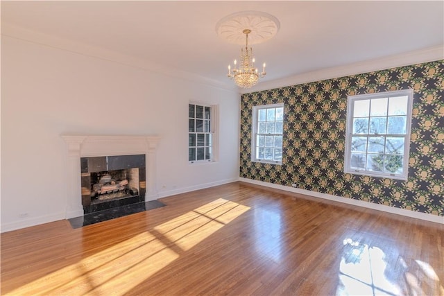 unfurnished living room featuring wood finished floors, baseboards, wallpapered walls, a fireplace with flush hearth, and a chandelier