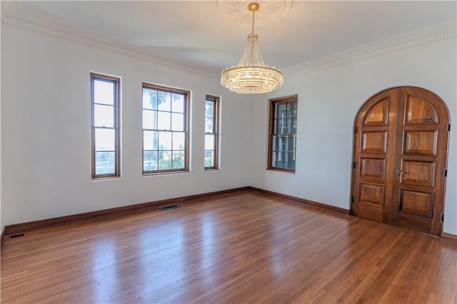 spare room with wood finished floors, baseboards, visible vents, ornamental molding, and a chandelier