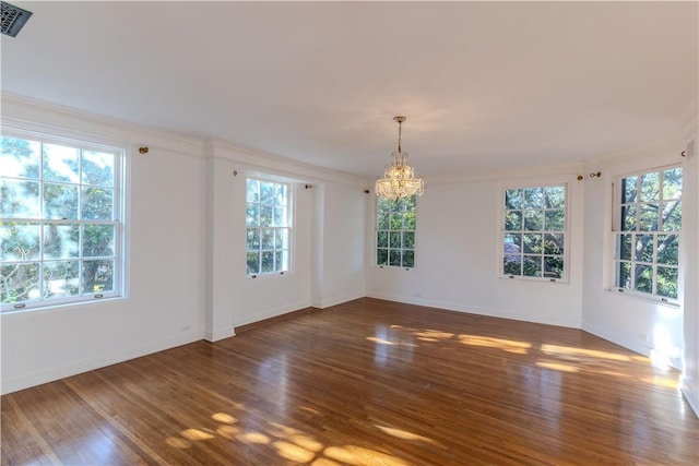 spare room featuring an inviting chandelier, crown molding, wood finished floors, and visible vents