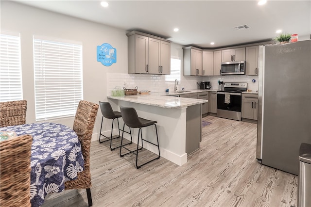 kitchen featuring a kitchen bar, kitchen peninsula, light hardwood / wood-style flooring, gray cabinets, and appliances with stainless steel finishes