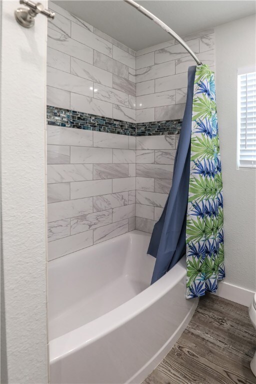 bathroom with toilet, shower / bath combo with shower curtain, and wood-type flooring