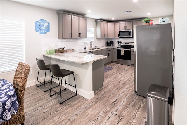 kitchen featuring stainless steel appliances, kitchen peninsula, sink, backsplash, and light wood-type flooring